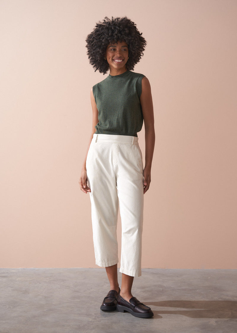 Woman wearing a green sleeveless top and light cream corduroy cropped trousers against a beige background