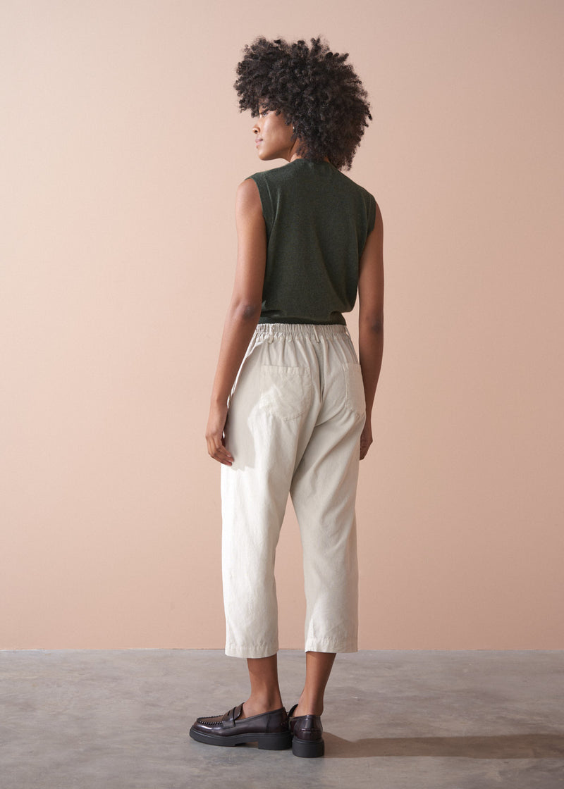 Person wearing a green sleeveless top and light cream corduroy cropped trousers against a beige background