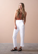 woman wearing a burn orange top with white tapered leg linen trousers