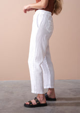 woman wearing a burn orange top with white tapered leg linen trousers and sandals