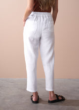 woman wearing a burn orange top with white tapered leg linen trousers and sandals