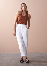 woman wearing a burn orange top with white tapered leg linen trousers
