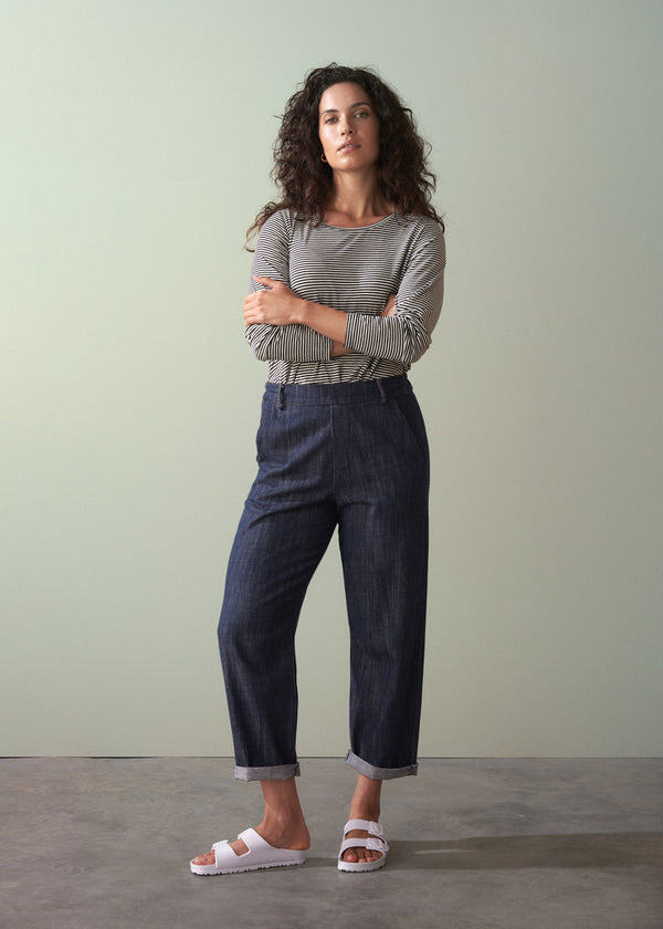 Woman wearing a striped shirt and dark jeans standing against a plain background