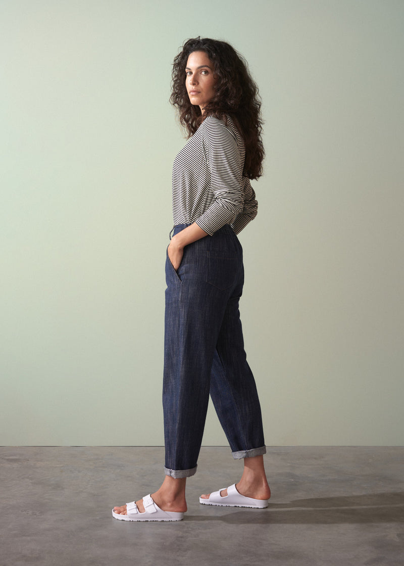 Woman wearing a striped shirt and dark jeans against a plain background