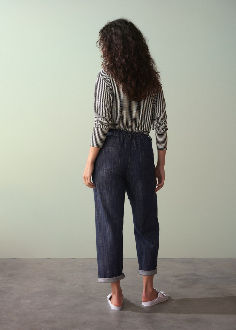 Woman wearing a striped shirt and dark jeans against a plain background