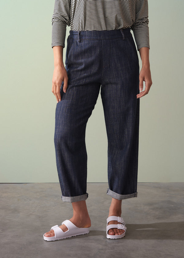 Person wearing dark blue jeans and white sandals on a plain background