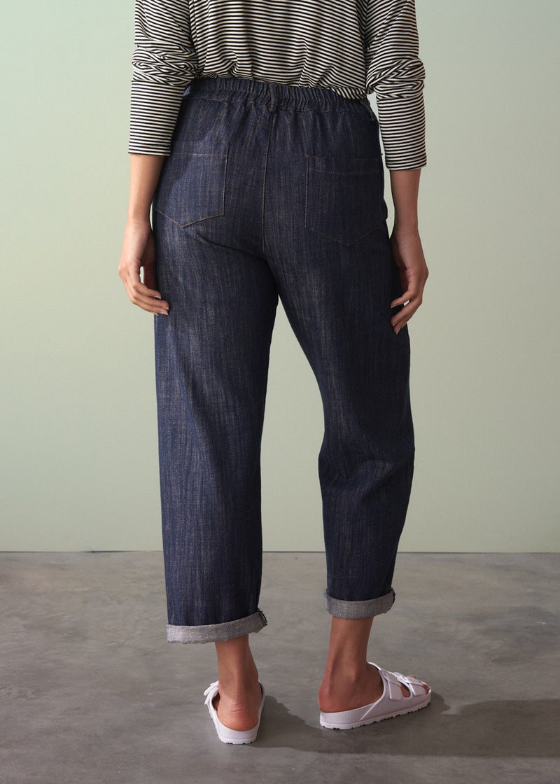 Person wearing dark blue denim jeans and a striped shirt against a plain background