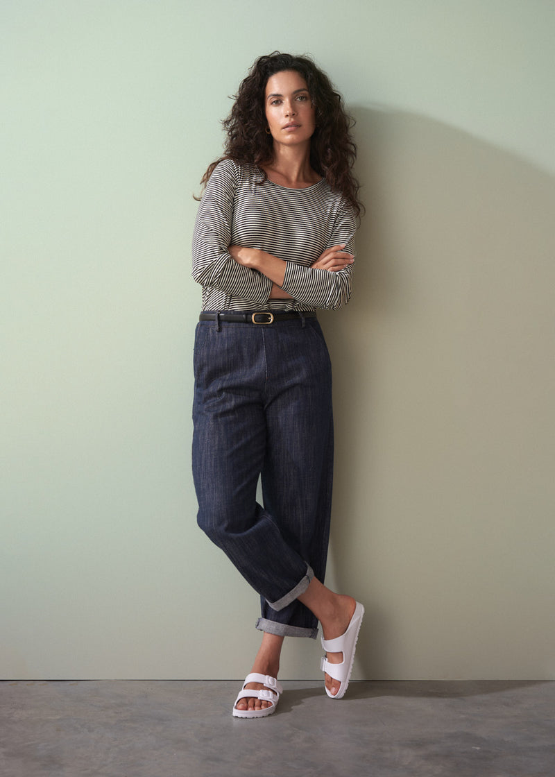 Woman wearing a striped shirt and jeans against a plain wall