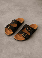 Pair of black sandals with brown soles on a gray concrete surface