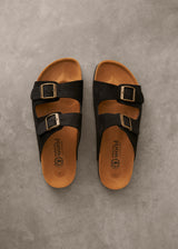 Pair of black sandals with brown soles on a gray surface