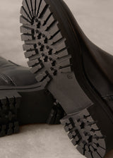 Close-up of black boots with tread pattern on a neutral background