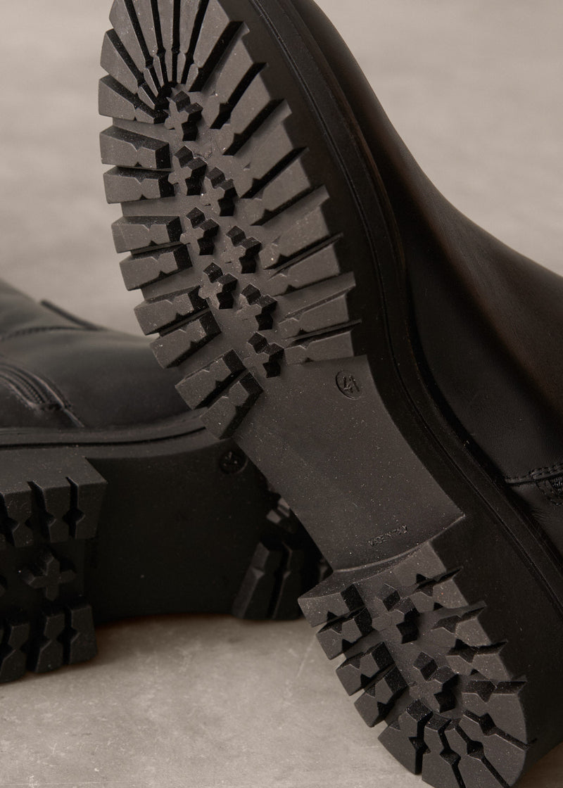 Close-up of black boots with tread pattern on a neutral background