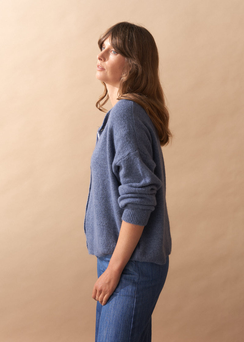 Model wearing light blue wool blend cardigan with mother of pearl buttons and wide leg jeans against a plain background