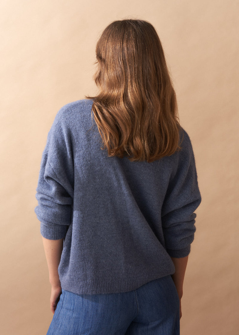 Model wearing light blue wool blend cardigan with mother of pearl buttons and wide leg jeans against a plain background