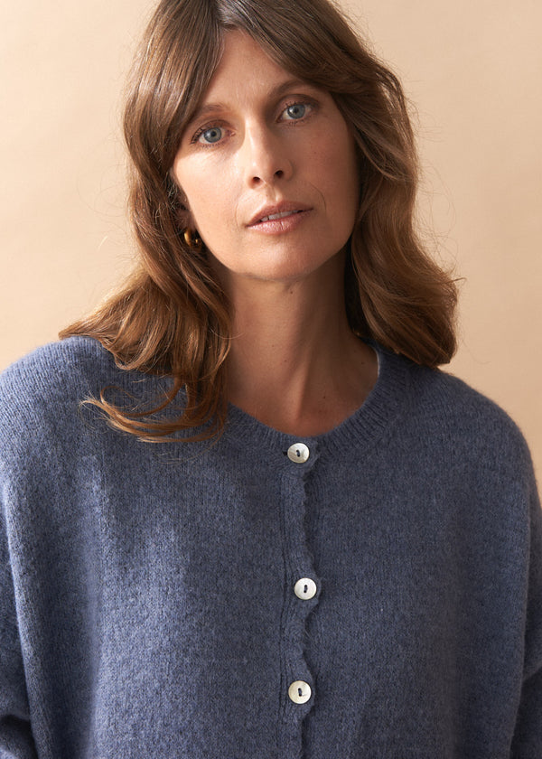 Model wearing light blue wool blend cardigan with mother of pearl buttons and wide leg jeans against a plain background