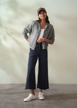 Woman wearing a grey wool cardigan over a white shirt and dark trousers on a plain background
