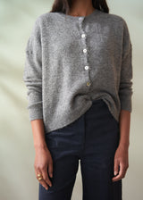Woman wearing a grey wool cardigan over a white shirt and dark trousers on a plain background