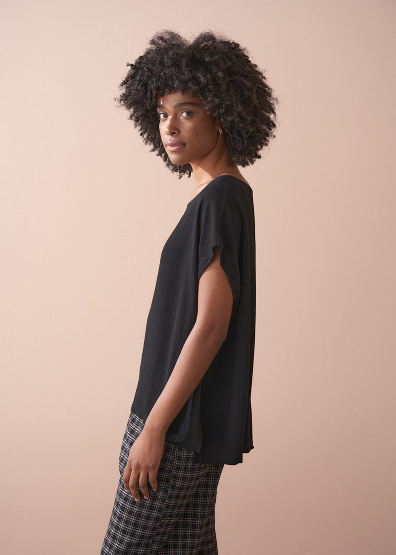 Woman wearing a black top and plaid barrel leg trousers against a beige background