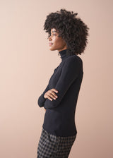Woman wearing a black turtleneck and plaid pants against a beige background