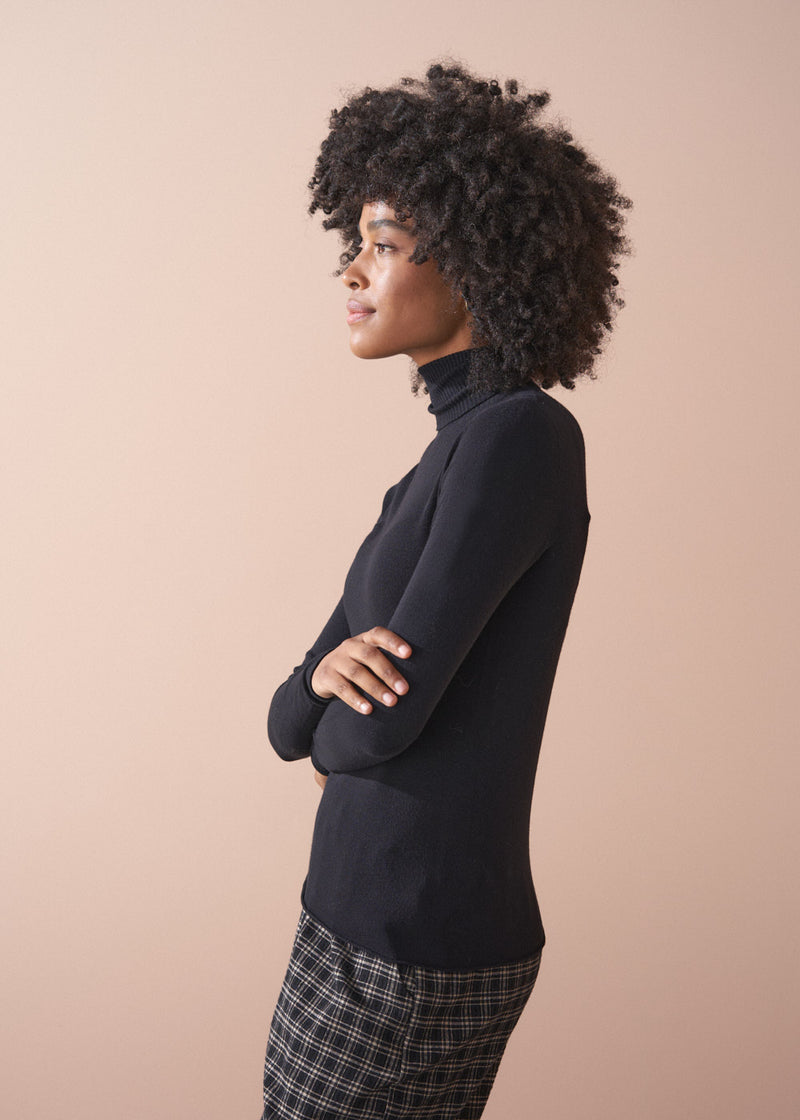 Woman wearing a black turtleneck and plaid pants against a beige background