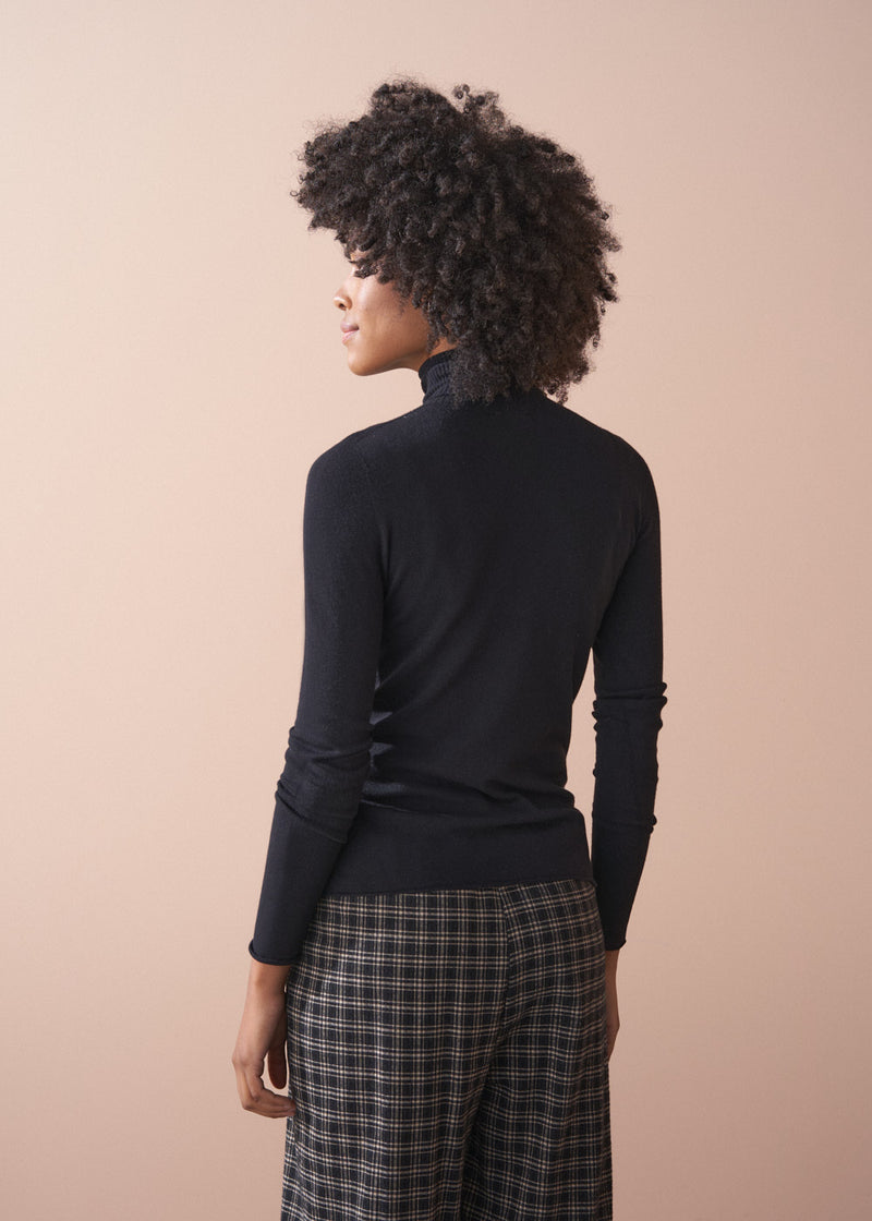 Person wearing a black turtleneck and plaid barrel leg trousers against a beige background