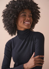 Woman wearing a black turtleneck sweater against a beige background