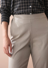 Woman wearing a black and white checkered shirt, beige slim fit trousers, and black boots against a beige background