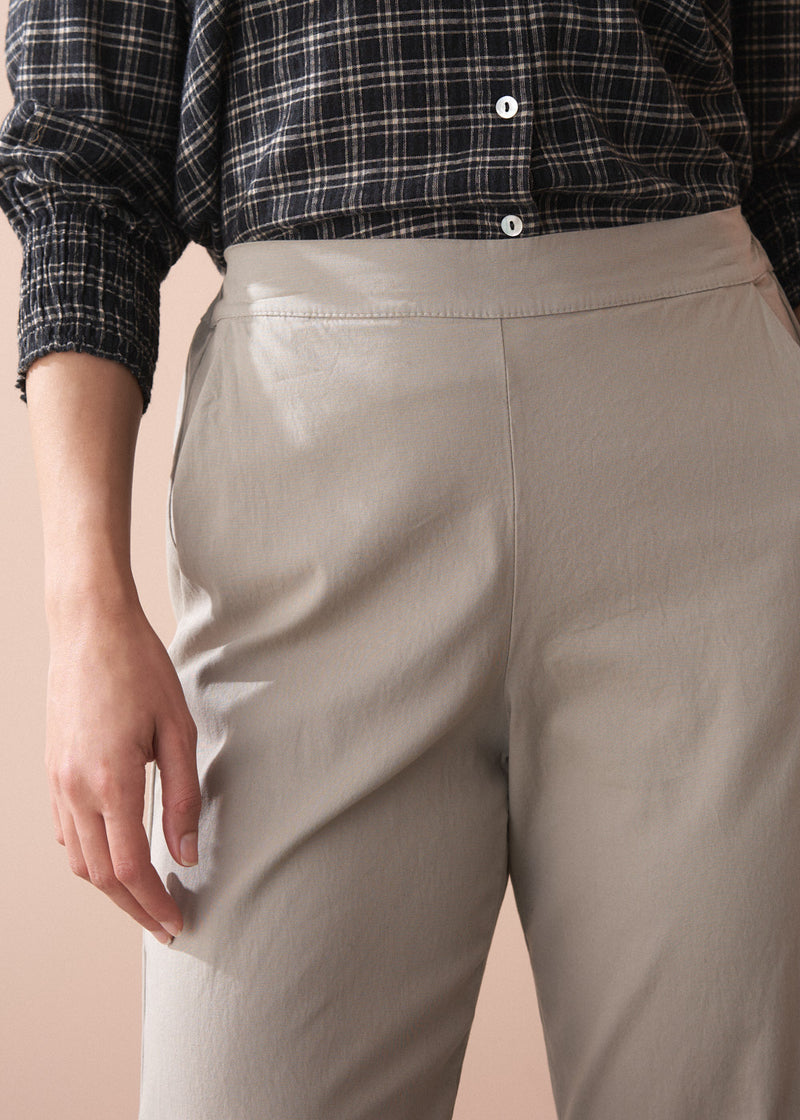 Woman wearing a black and white checkered shirt, beige slim fit trousers, and black boots against a beige background