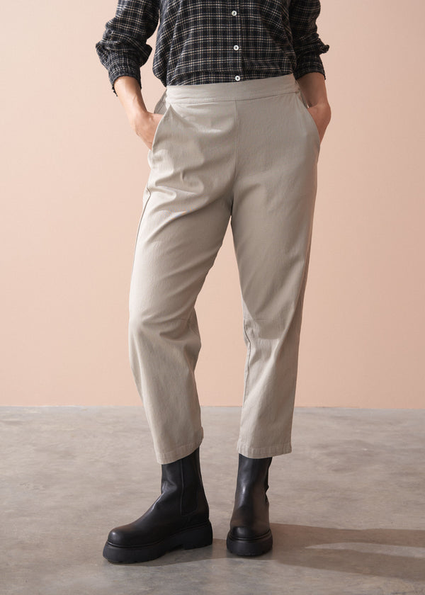 Woman wearing a black and white checkered shirt, beige slim fit trousers, and black boots against a beige background