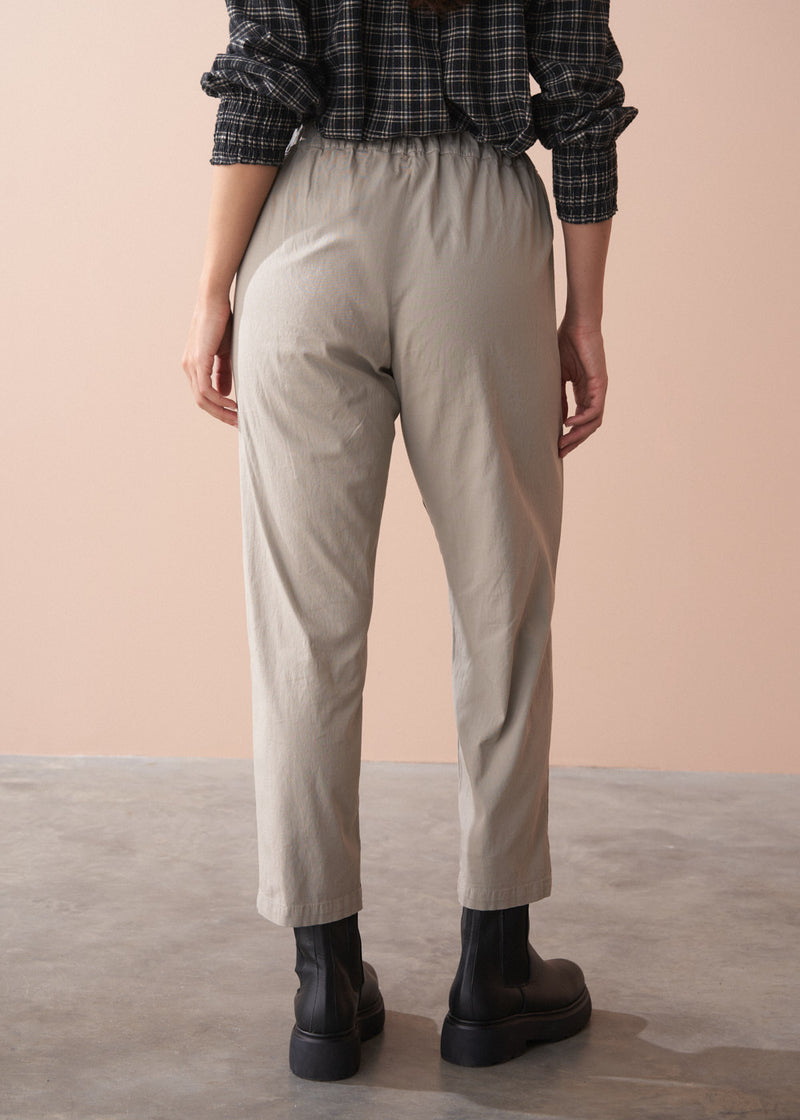 Woman wearing a black and white checkered shirt, beige slim fit trousers, and black boots against a beige background