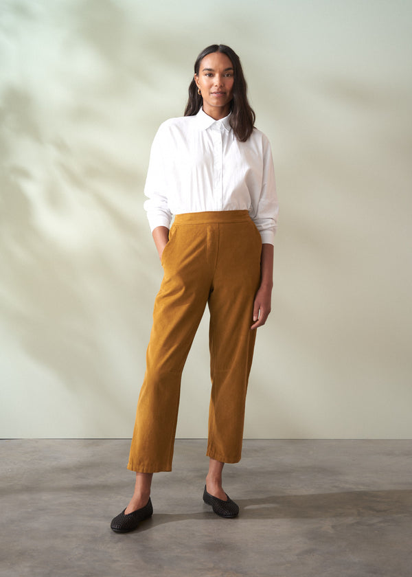 Woman wearing a white shirt and mustard yellow corduroy trousers against a plain background