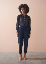 Person wearing a navy shirt and navy corduroy trousers against a beige background