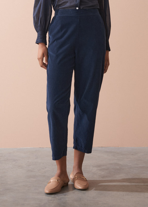 Person wearing navy corduroy trousers and brown shoes on a beige background