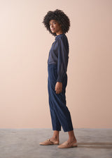 Woman wearing a dark blue blouse and navy corduroy trousers against a beige background