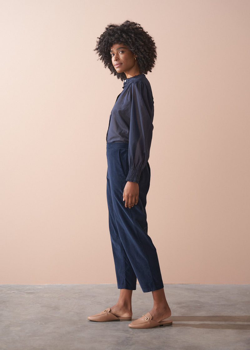 Woman wearing a dark blue blouse and navy corduroy trousers against a beige background
