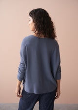Woman wearing a grey sweater and dark pants against a beige background