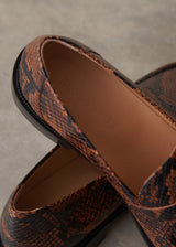 Close-up of a pair of slip-on loafers with a brown and black snakeskin pattern, showing the textured upper, black sole, and tan insole with the brand name 'RUSSET & FOX' printed on it.