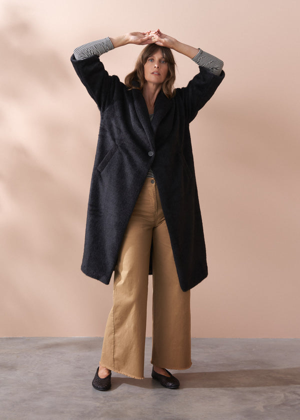 Woman wearing a black fur coat and neutral wide leg trousers against a beige background