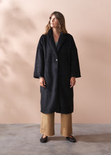 Woman wearing a black fur coat and neutral wide leg trousers against a beige background