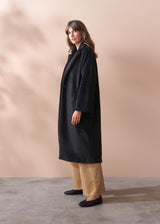 Woman wearing a black fur coat and neutral wide leg trousers against a beige background