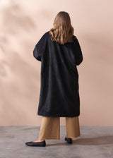 Woman wearing a black fur coat and neutral wide leg trousers against a beige background