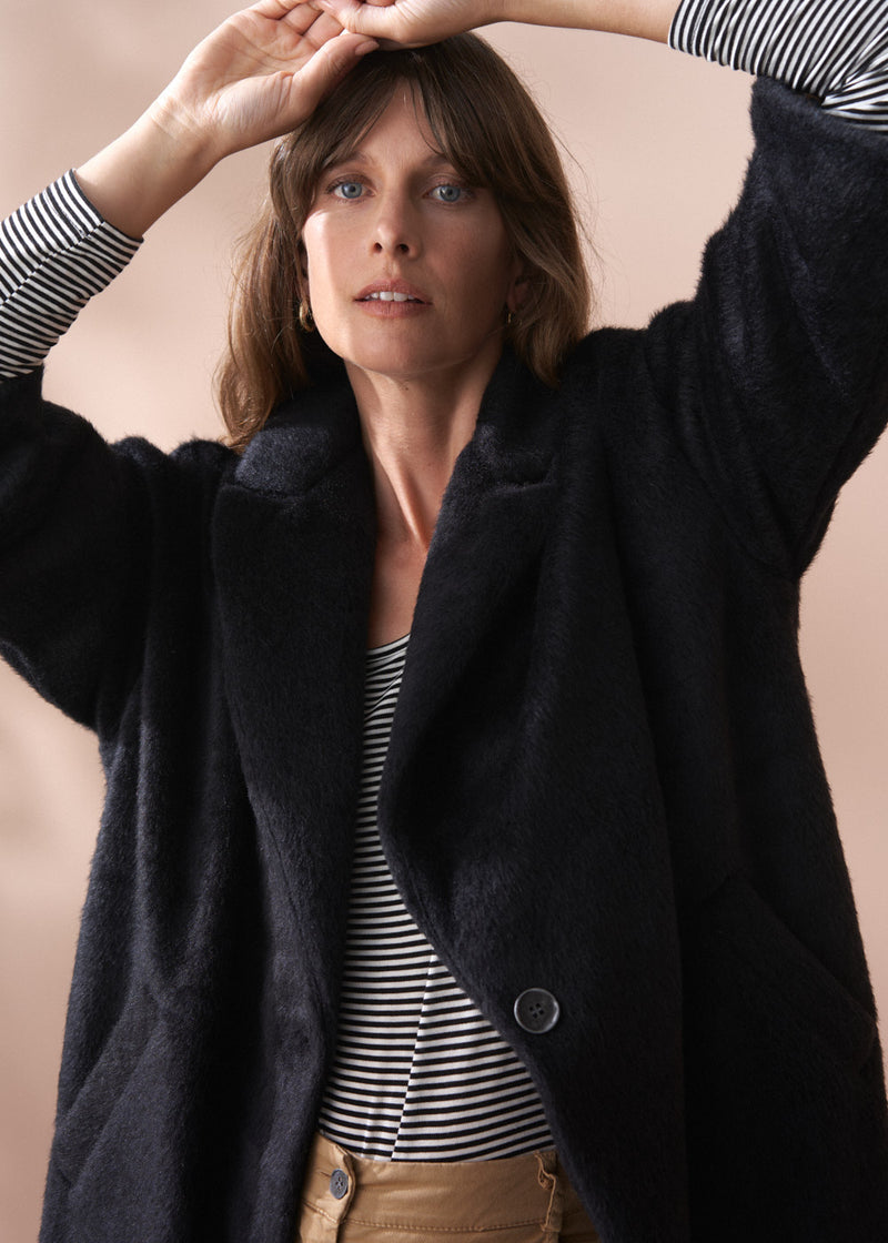 Woman wearing a black fur coat and neutral wide leg trousers against a beige background