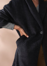 Woman wearing a black fur coat and neutral wide leg trousers against a beige background