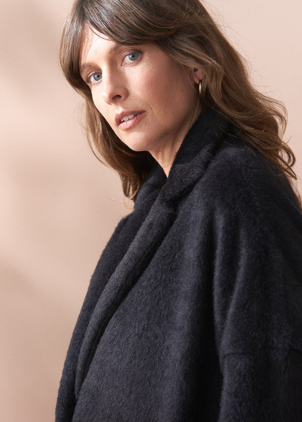 Woman wearing a black fur coat and neutral wide leg trousers against a beige background