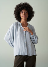 Woman wearing a light blue shirt and dark green trousers with a plain background