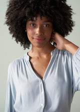 Woman wearing a light blue shirt and dark green trousers with a plain background