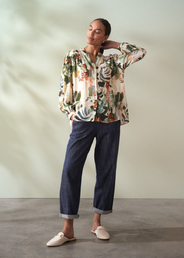 Woman wearing a floral blouse and dark pants against a plain background