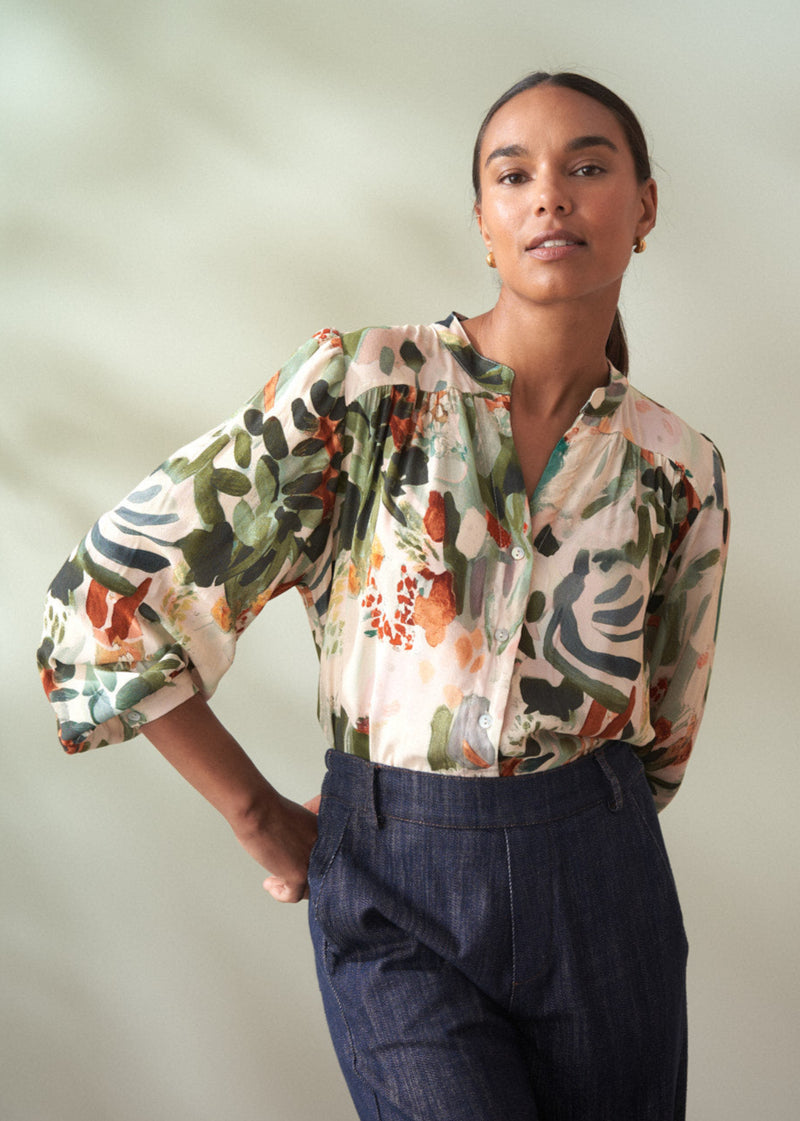 Woman wearing a floral blouse with puffed sleeves and dark pants against a plain background