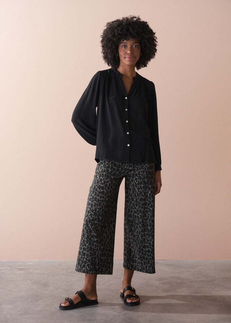 Woman wearing a black blouse and patterned pants against a beige background