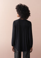 Person wearing a black blouse with long sleeves on a beige background